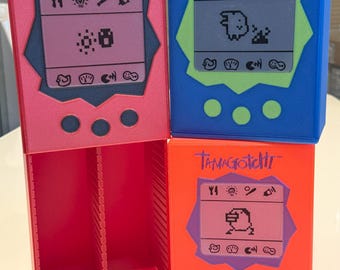 May include: Three Tamagotchi digital pet toys. One is pink, one is blue, and one is orange. Each toy has a screen with a pixelated image of a pet and buttons for interacting with the pet. The toys are all in a new condition.