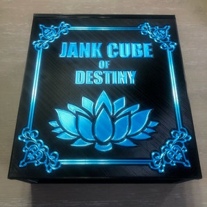 Könnte beinhalten: Eine schwarze Box mit einem blauen und silbernen Design. Die Box hat eine blaue Lotusblume in der Mitte und den Text "Jank Cube of Destiny" oben.