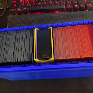 Puede incluir: Una caja de almacenamiento de tarjetas de plástico azul con tres compartimentos. Los compartimentos están llenos de tarjetas negras, moradas y rojas.