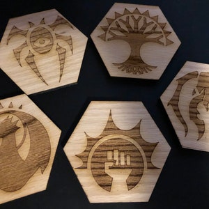 May include: Five wooden hexagonal coasters with different symbols burned into the surface. The symbols include a spider, a tree, a dragon, a fist, and a creature with claws.