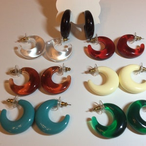 May include: A collection of colorful, crescent-shaped earrings in various hues, including black, clear, red, amber, cream, turquoise, and green. Each pair features a post-back closure, offering a stylish and versatile accessory option.