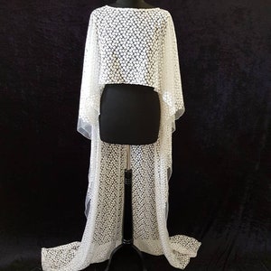 May include: White lace bridal cape with a scalloped hem and a delicate floral pattern. The cape is displayed on a dress form.