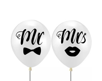 May include: Two white balloons with black lettering. One balloon says "Mr." with a bow tie and the other says "Mrs." with a red lip.