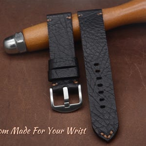 May include: Black leather watch strap with a silver buckle. The strap has a textured surface and is stitched with light brown thread. The text "Custom Made For Your Wrist" is visible at the bottom of the image.