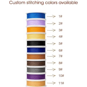 May include: A vertical stack of eleven spools of thread in various colors, including blue, lavender, orange, yellow, black, dark blue, brown, dark brown, gray, purple, and tan. The text Custom stitching colors available is at the top.