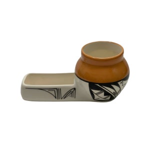 May include: A white ceramic planter with a black geometric design. The planter has a separate section for a small plant and a larger section for a larger plant. The larger section is orange with a black geometric design.