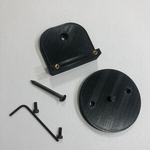 May include: A black 3D-printed mounting bracket kit. The kit includes a curved bracket with brass inserts, a circular base, a screw, two bolts, and an Allen wrench. The parts are arranged on a white surface.