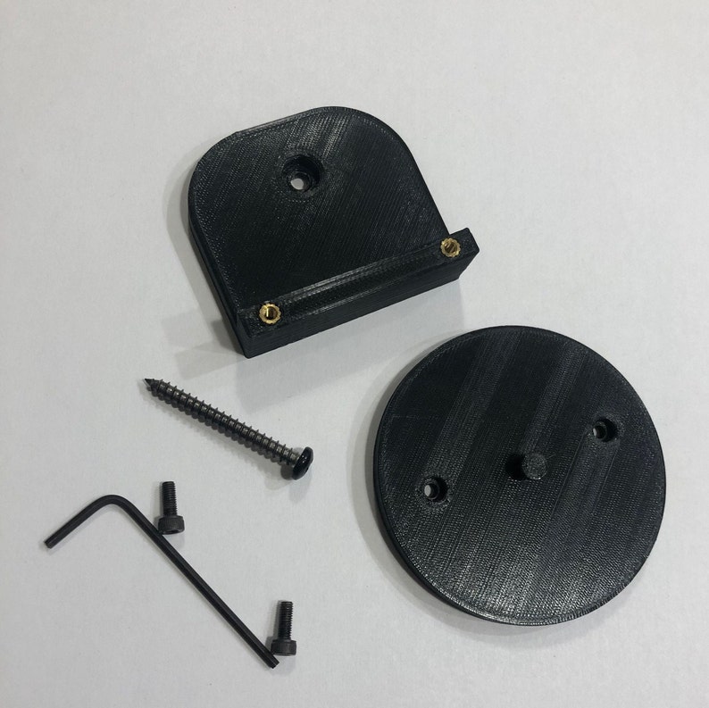 May include: A black 3D-printed mounting bracket kit. The kit includes a curved bracket with brass inserts, a circular base, a screw, two bolts, and an Allen wrench. The parts are arranged on a white surface.