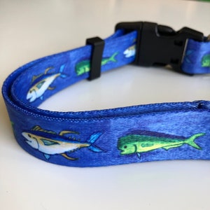 May include: Blue dog collar with a colorful fish print. The collar has a black plastic buckle.