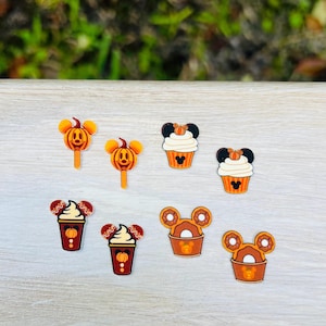 May include: A set of six Halloween-themed earrings featuring Mickey Mouse ears. The earrings are made of acrylic and feature various fall-themed treats, including a pumpkin lollipop, a cupcake, a coffee cup, and a donut.