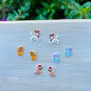 May include: A set of six cartoon dog earrings. The earrings feature a white and brown dog with a red collar, a white and brown dog with a red collar, a brown and orange dog with a red collar, a brown and orange dog with a red collar, a light blue dog with a pink bow, and a light blue dog with a pink bow.