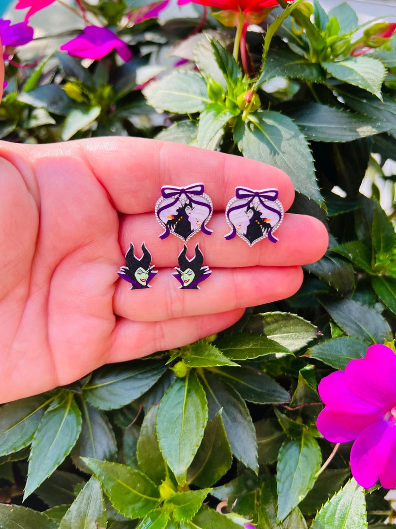 Puede incluir: Un conjunto de cuatro pendientes con el personaje Mal&eacute;fica de la pel&iacute;cula de Disney La Bella Durmiente. Los pendientes son de plata con detalles en morado y negro. Dos pendientes muestran la cara de Mal&eacute;fica, y dos pendientes muestran a Mal&eacute;fica en su forma de drag&oacute;n.