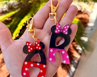 May include: Two acrylic letter keychains, an "A" and an "R", in a Minnie Mouse theme. The letters are black and red with white polka dots, and feature gold-colored clasps. Each letter has a bow with white polka dots.