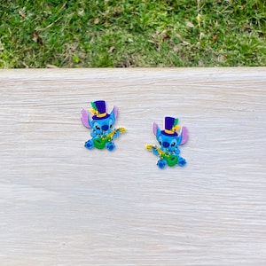 Puede incluir: Dos figuras azules de personajes de dibujos animados, cada una con un sombrero de copa morado con una pluma verde y tocando un ukelele verde. Las figuras tienen orejas grandes y sostienen el ukelele con cuerdas amarillas.