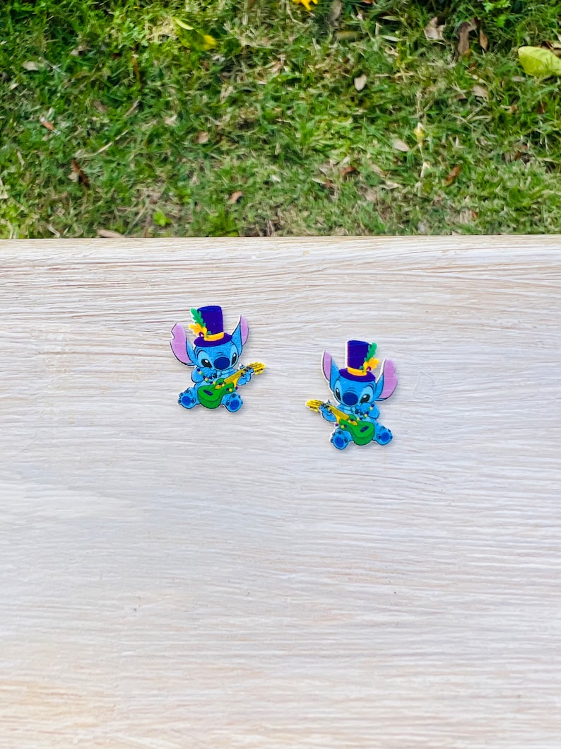 Puede incluir: Dos figuras azules de personajes de dibujos animados, cada una con un sombrero de copa morado con una pluma verde y tocando un ukelele verde. Las figuras tienen orejas grandes y sostienen el ukelele con cuerdas amarillas.