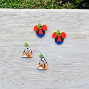 May include: Four colorful cartoon character charms. Two charms are shaped like Mickey Mouse's head, with red ears, a black face, a blue bottom, and a green hat. Two charms depict Goofy in an orange outfit and a green hat.