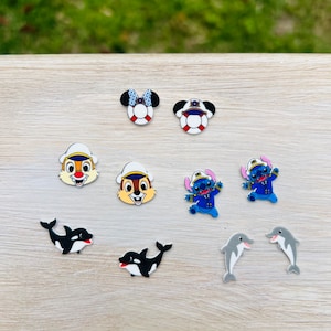 May include: A collection of colorful cartoon character charms, including Mickey and Minnie Mouse, Chip and Dale, Stitch, orcas, and dolphins. The charms feature various colors and designs, perfect for adding to shoes or accessories.
