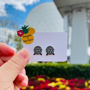 May include: A pair of black and white geometric sphere stud earrings. The earrings are displayed on a white card with a pineapple and flower sticker that reads "Pineapples & Pixie Dust co."