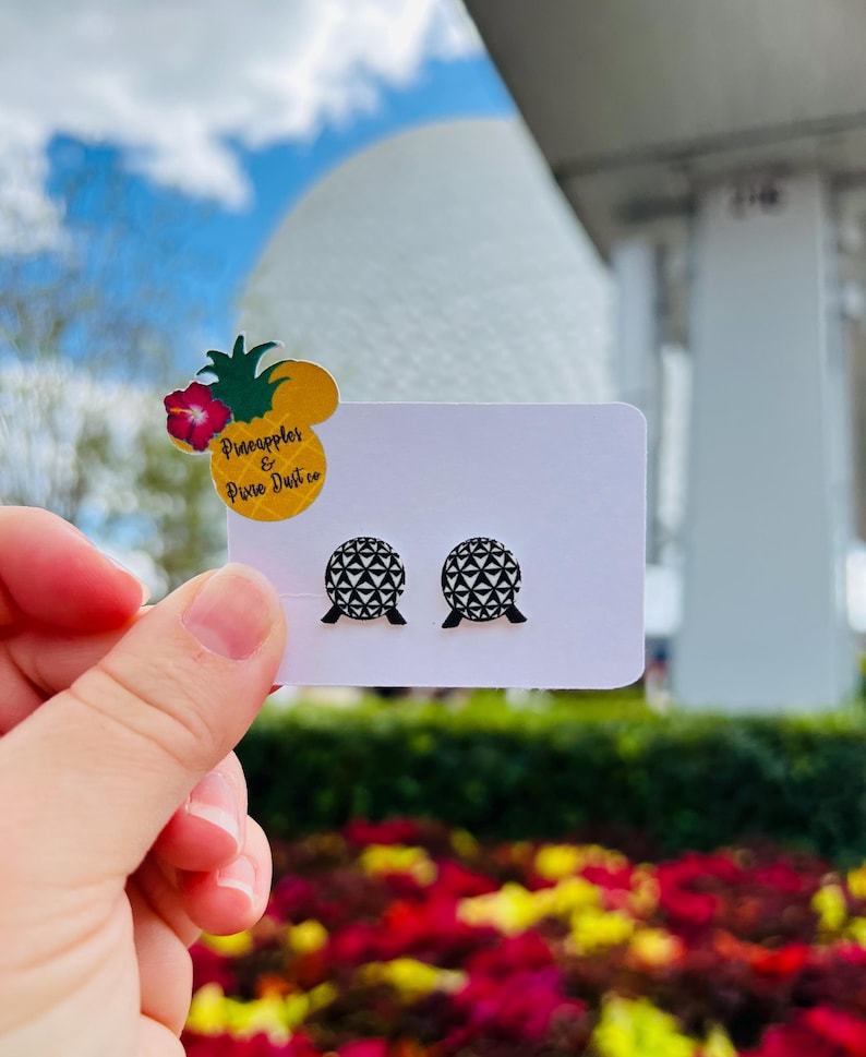 May include: A pair of black and white geometric sphere stud earrings. The earrings are displayed on a white card with a pineapple and flower sticker that reads "Pineapples & Pixie Dust co."