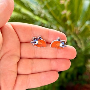 May include: A pair of stud earrings featuring the cartoon character Zazu from The Lion King. Each earring displays the bird's head with a prominent orange beak, blue feathers, and a distinct facial expression with dark eyebrows and a small smile.
