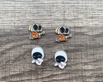 May include: Four small character charms. Two are beige with black eyes and orange details, resembling a robot. The other two are white with black faces, blue eyes, and a red heart, resembling a character from a movie.