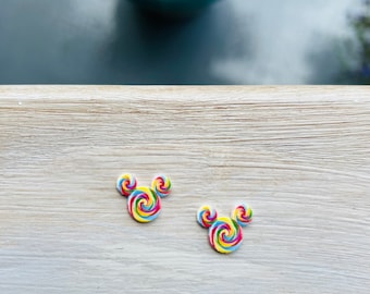 May include: Two colorful, swirl-patterned Mickey Mouse-shaped embellishments. The embellishments feature a rainbow of colors, including yellow, blue, green, and pink. They are placed on a light wood-grain surface.