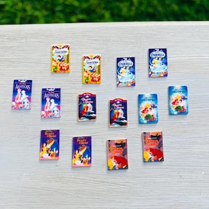May include: A collection of miniature VHS tapes featuring classic animated films like "Snow White," "Cinderella," "The Aristocats," "The Sword in the Stone," "Beauty and the Beast," "Sleeping Beauty," and "The Little Mermaid." The tapes have colorful artwork.