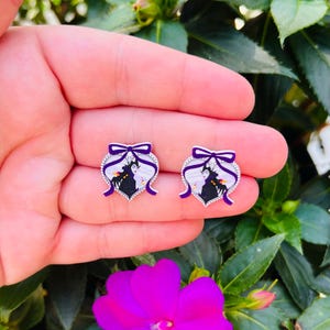 Puede incluir: Un par de pendientes de plata en forma de coraz&oacute;n con un lazo morado y una imagen en blanco y negro de Mal&eacute;fica y Aurora de la pel&iacute;cula de Disney La Bella Durmiente.