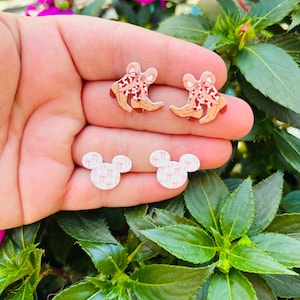May include: A pair of pink and brown cowboy boot earrings and a pair of white Mickey Mouse earrings with a pink and white pattern.
