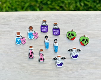 May include: A collection of whimsical, colorful potion bottle and apple-shaped charms. The bottles feature various designs, including labels that read "Deadly Nightshade" and "Drink Me." The apples are green with red accents.