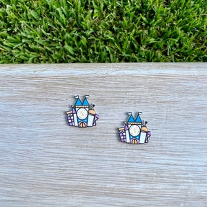 May include: Two enamel pins featuring a cartoon illustration of a castle with blue, purple, and yellow accents. The castle has a clock tower with a gold "C" inside.