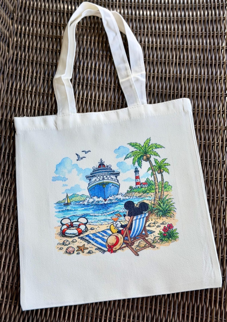May include: Off-white canvas tote bag featuring a colorful beach scene with a cruise ship, palm trees, and a lighthouse. Mickey Mouse is relaxing in a beach chair. The bag has white handles.