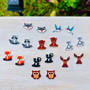 May include: A collection of colorful, felt animal shapes, including raccoons, hummingbirds, bears, foxes, skunks, owls, wolves, and moose. The shapes are arranged on a light-colored wooden surface, perfect for crafting or embellishing projects.