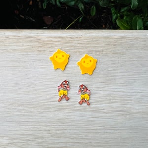 May include: A pair of yellow star-shaped earrings and a pair of brown and yellow cartoon dog earrings.