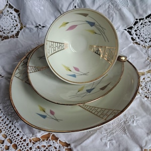 Könnte beinhalten: Ein Vintage-Tee-Set. Das cremefarbene Porzellan hat einen goldenen Rand und ein geometrisches Design mit farbigen Akzenten. Das Set beinhaltet eine Teetasse, eine Untertasse und einen größeren Teller.