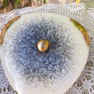 Peut inclure: Un plat en céramique blanche avec un bord doré et un bouton doré au centre. Le plat a un glaçage craquelé et un motif moucheté.