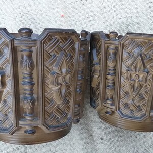 May include: Two brown, decorative, round plant pots with intricate carved designs. The pots are made of a textured material and have a slightly raised rim.