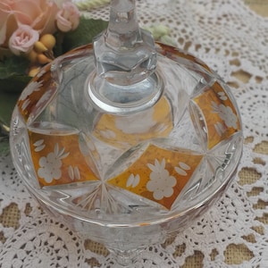 Op de afbeelding: Een glazen snoepvaasje met een gouden ontwerp en gegraveerde bloemmotieven. De vaas heeft een deksel met een knop bovenop.