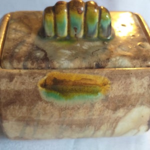 Può includere: Una scatola in ceramica con un coperchio che presenta un design decorativo astratto multicolore. La scatola ha una smaltatura marrone, bianca e verde con un accento giallo.