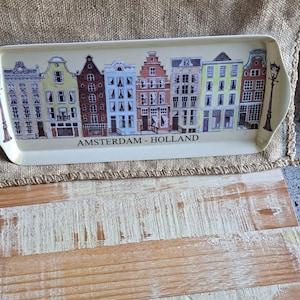 Könnte beinhalten: Rechteckiges Serviertablett mit cremefarbenem Rand und einer farbenfrohen Illustration von Amsterdamer Grachtenhäusern. Das Tablett trägt den Text "AMSTERDAM - HOLLAND" und eine dekorative Straßenlaterne.