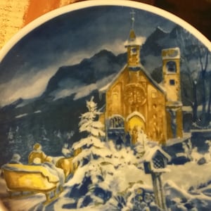 Könnte beinhalten: Ein antiker Keramikteller mit einer Winterszene, die eine Kirche, schneebedeckte Bäume und einen von einem Pferd gezogenen Schlitten zeigt. Die Kirche ist mit warmem gelbem Licht beleuchtet, was eine festliche Atmosphäre schafft.