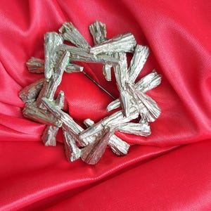 May include: A silver brooch with a geometric design, resembling a starburst or a flower, on a red fabric background.