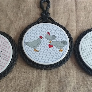 Peut inclure: Trois dessous-de-plat en fonte noire avec des inserts en céramique blanche. Chaque dessous-de-plat présente un motif d'animal de ferme différent : une vache, des poulets et des canards. Les dessous-de-plat ont un motif hexagonal.
