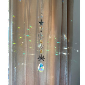 Puede incluir: Un atrapasol de cristal con un cristal en forma de lágrima, un sol, una luna y estrellas plateadas, y una cadena plateada.