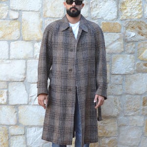 May include: A long brown and black plaid coat with a button-up front. The coat is worn over a white shirt and blue jeans. The person is wearing brown leather boots and sunglasses.