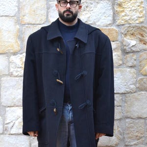 May include: A navy blue hooded duffel coat with a toggle fastening and four large pockets. The coat has a relaxed fit and is made of a thick, warm fabric.