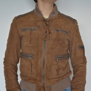May include: A brown suede bomber jacket with multiple pockets and a zipper closure. The jacket has a ribbed knit collar, cuffs, and waistband.
