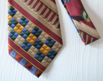 Puede incluir: Una corbata de seda con estampado geométrico en rojo, marrón, azul, amarillo y verde. La corbata tiene un ancho estrecho y una punta puntiaguda.