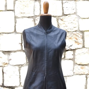 May include: A black leather vest with a zipper closure and two pockets. The vest is sleeveless and has a slightly flared hem.