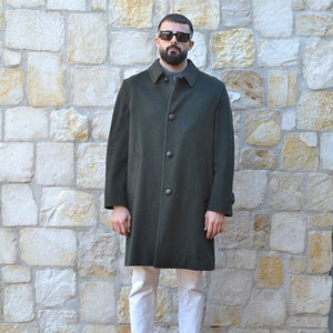 May include: A long dark green coat with a button fastening. The coat is worn over white trousers and brown boots.